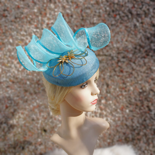 A blue hat with aqua blue crinoline trimmings and gold rhinestone petals on a blonde model