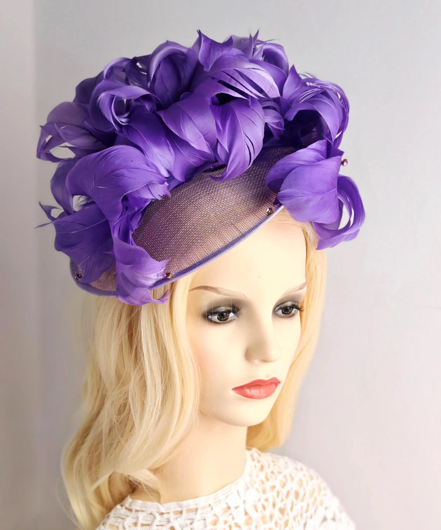 A large purple fascinator hat with layered ruffled fabric and a sheer mesh band, displayed on a blonde mannequin head against a plain light background.