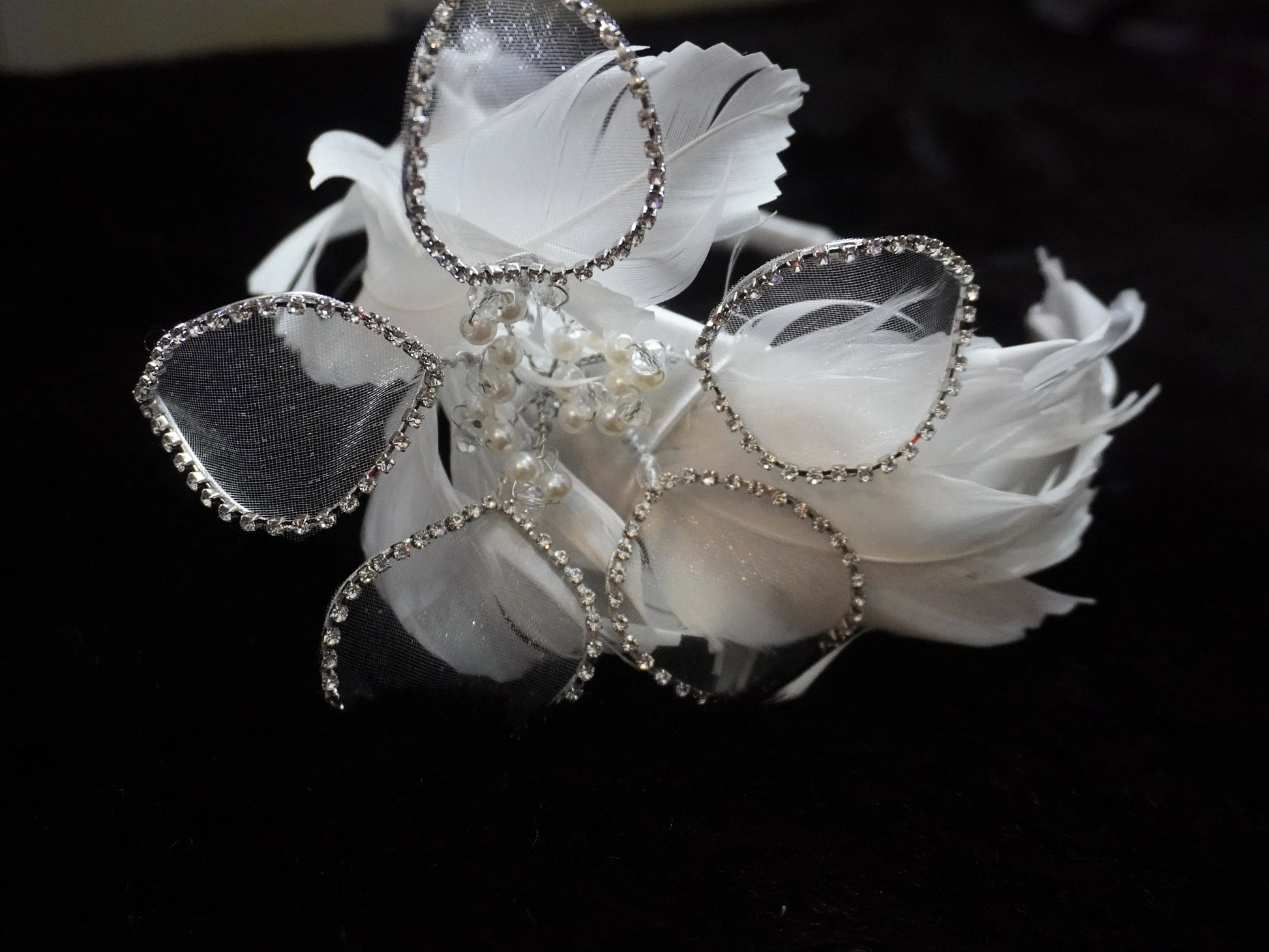 White feather fascinator headpiece with silver rhinestone trim and pearl accents, displayed on a black background.